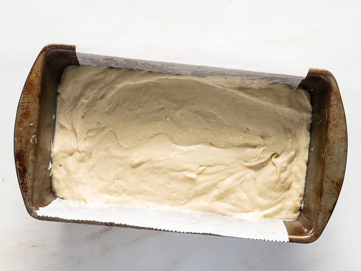 A loaf pan lined with parchment paper filled with smooth, unbaked batter on a light-colored surface.