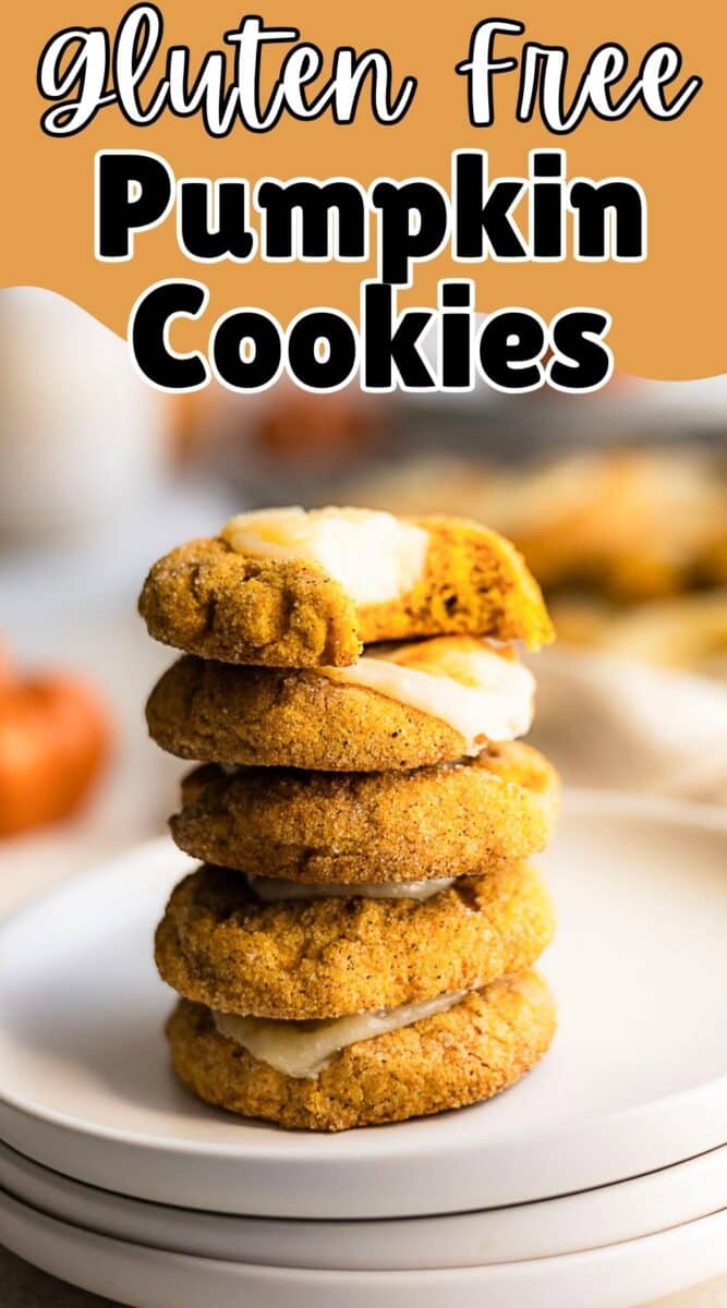 A stack of five gluten free pumpkin cookies with frosting sits on a white plate, while more cookies and a pumpkin are blurred in the background.