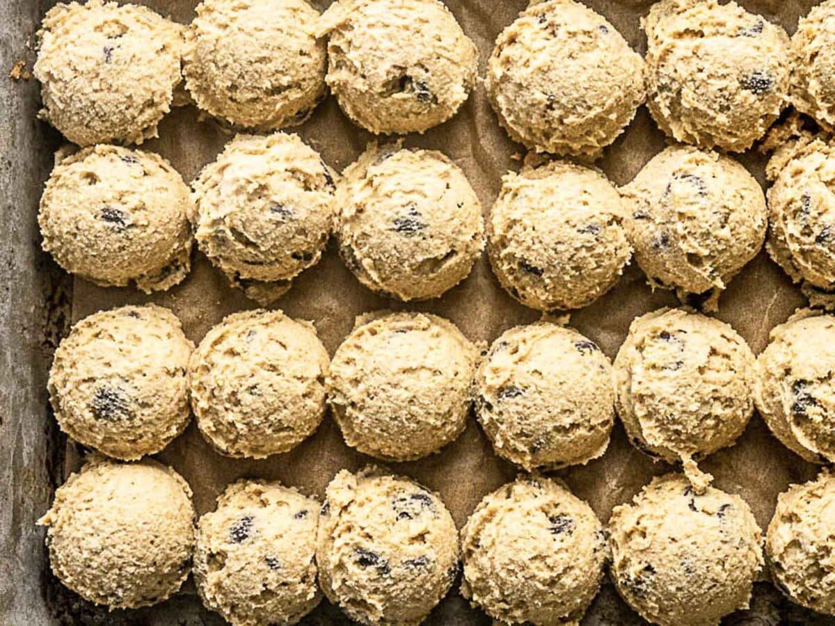 Rows of evenly spaced scoops of cookie dough with chocolate chips on a parchment-lined baking sheet.
