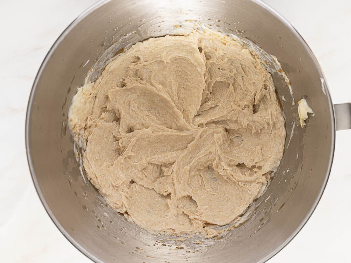 A metal mixing bowl containing creamed butter and sugar mixture, with a smooth, light brown texture.