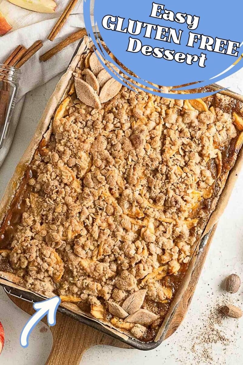 A baked gluten-free caramel apple pie crumble dessert in a rectangular dish with a crumbly topping, wooden spoon, and cinnamon sticks beside it. Text reads "Easy Gluten Free Dessert.