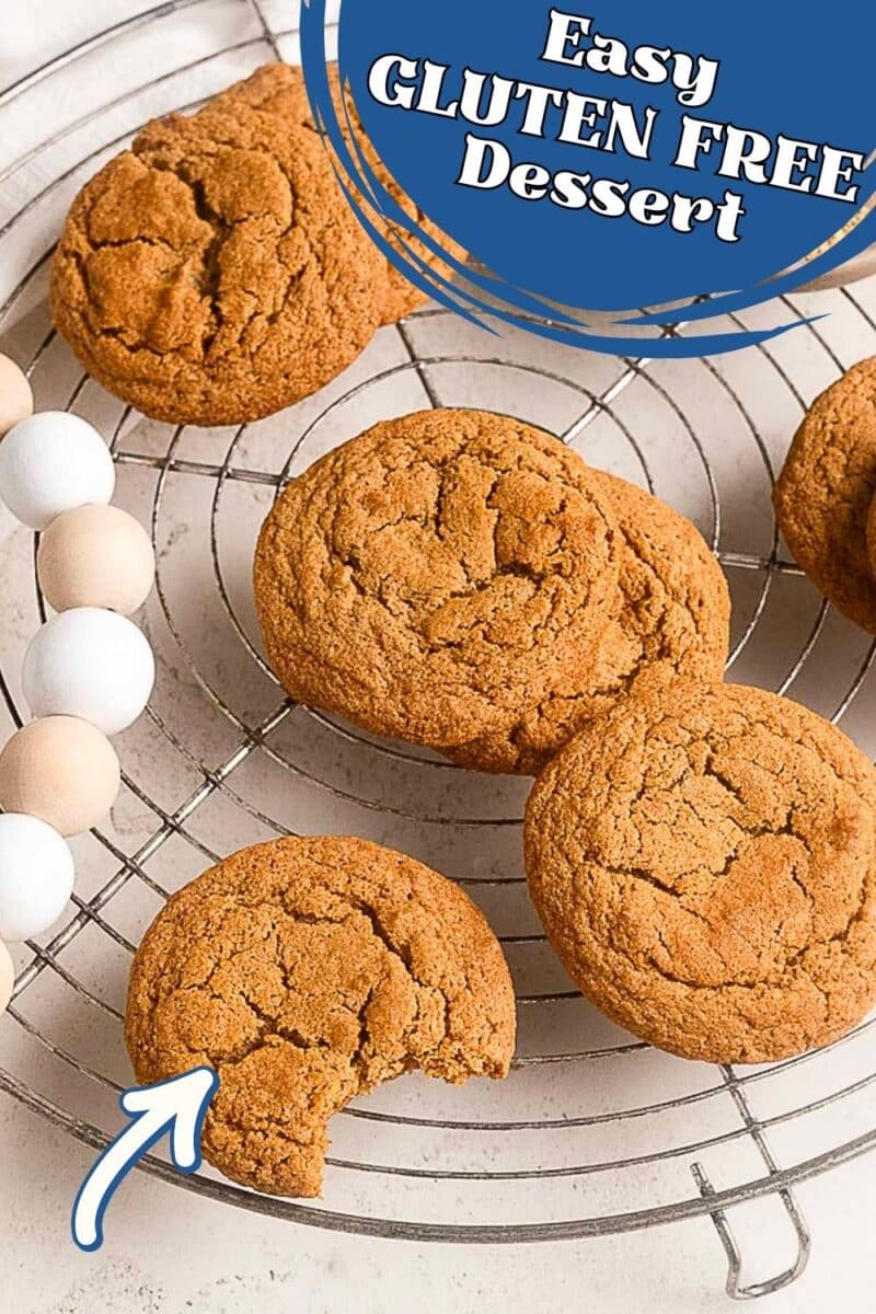 Four golden brown gluten free ginger snaps on a round cooling rack, with one cookie partially eaten.