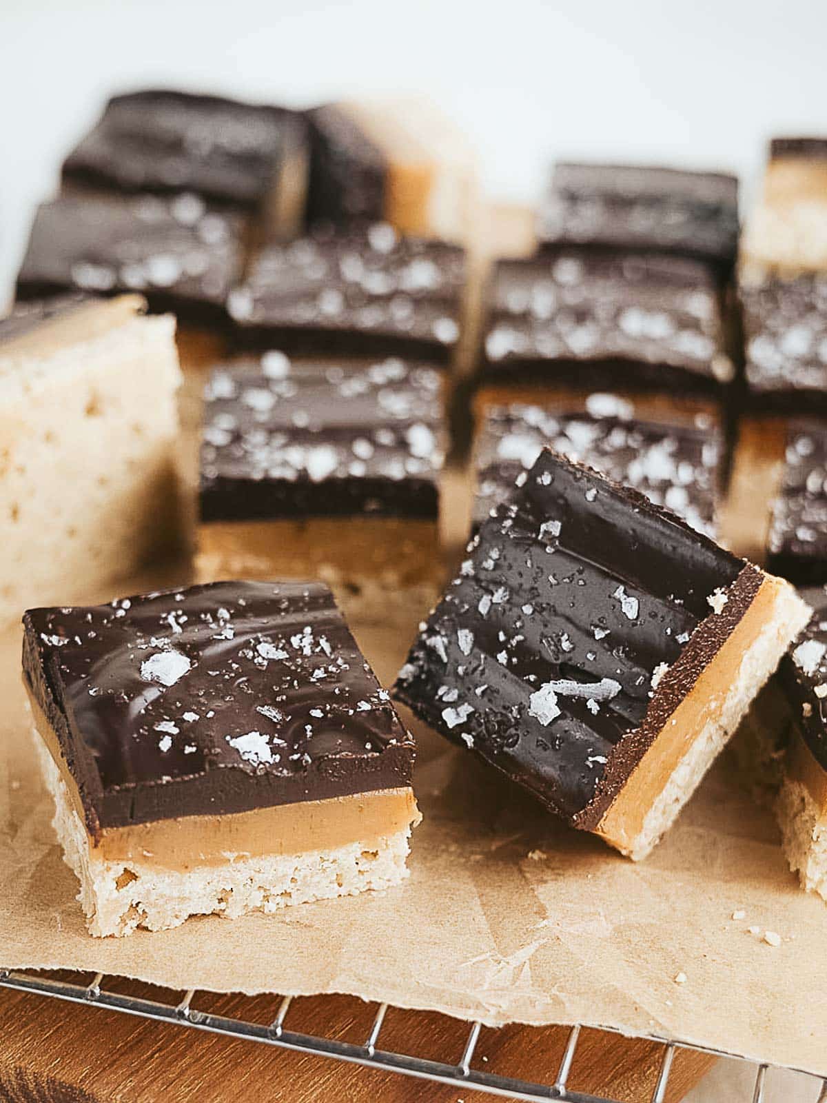 Squares of chocolate and caramel layered bars with a sprinkling of sea salt on top, arranged on parchment paper.