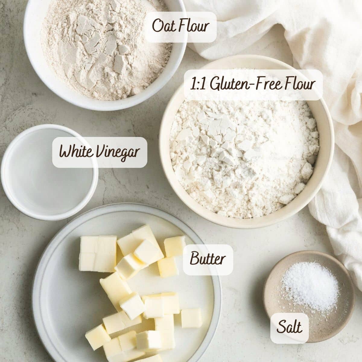 Bowls and plates with oat flour, 1:1 gluten-free flour, white vinegar, cubed butter, and salt are arranged on a light surface-perfect for making a delicious gluten free caramel apple pie.