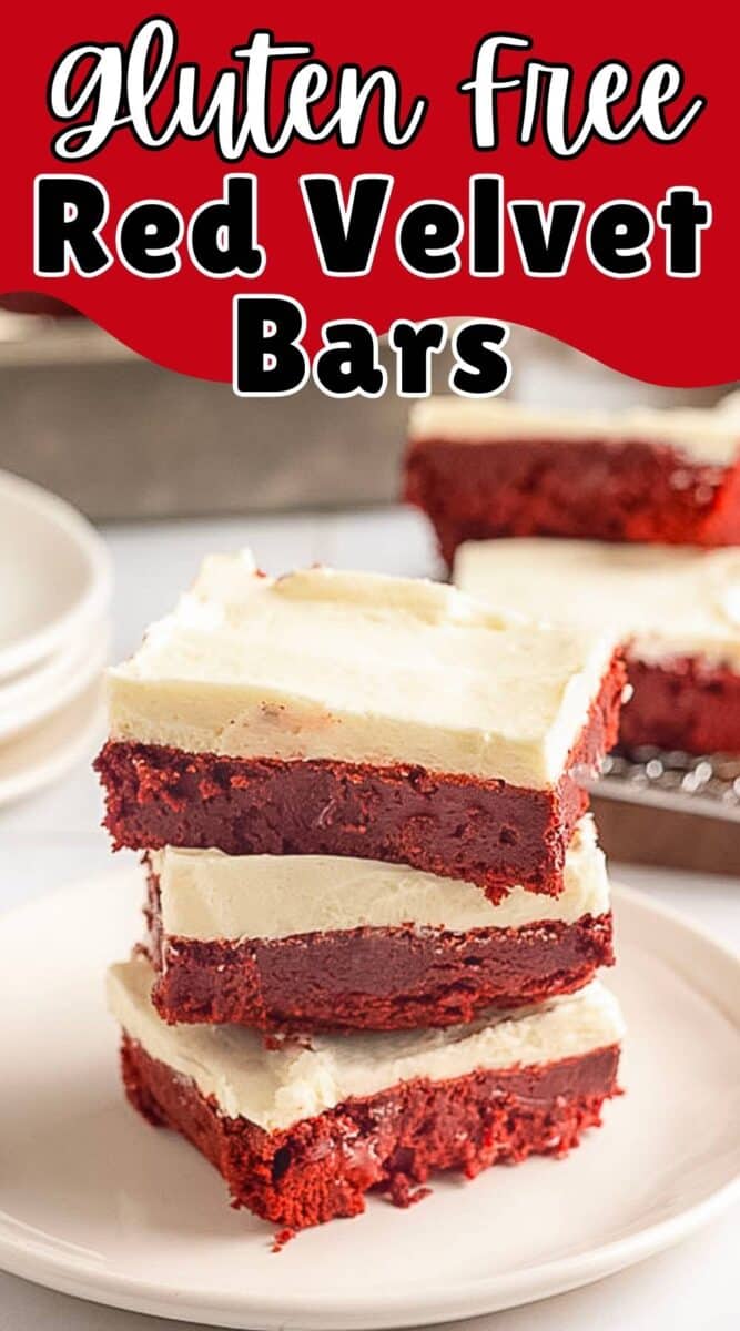 Three Gluten Free Red Velvet Brownies with a cream cheese layer are stacked on a plate, with more brownies and plates in the background.