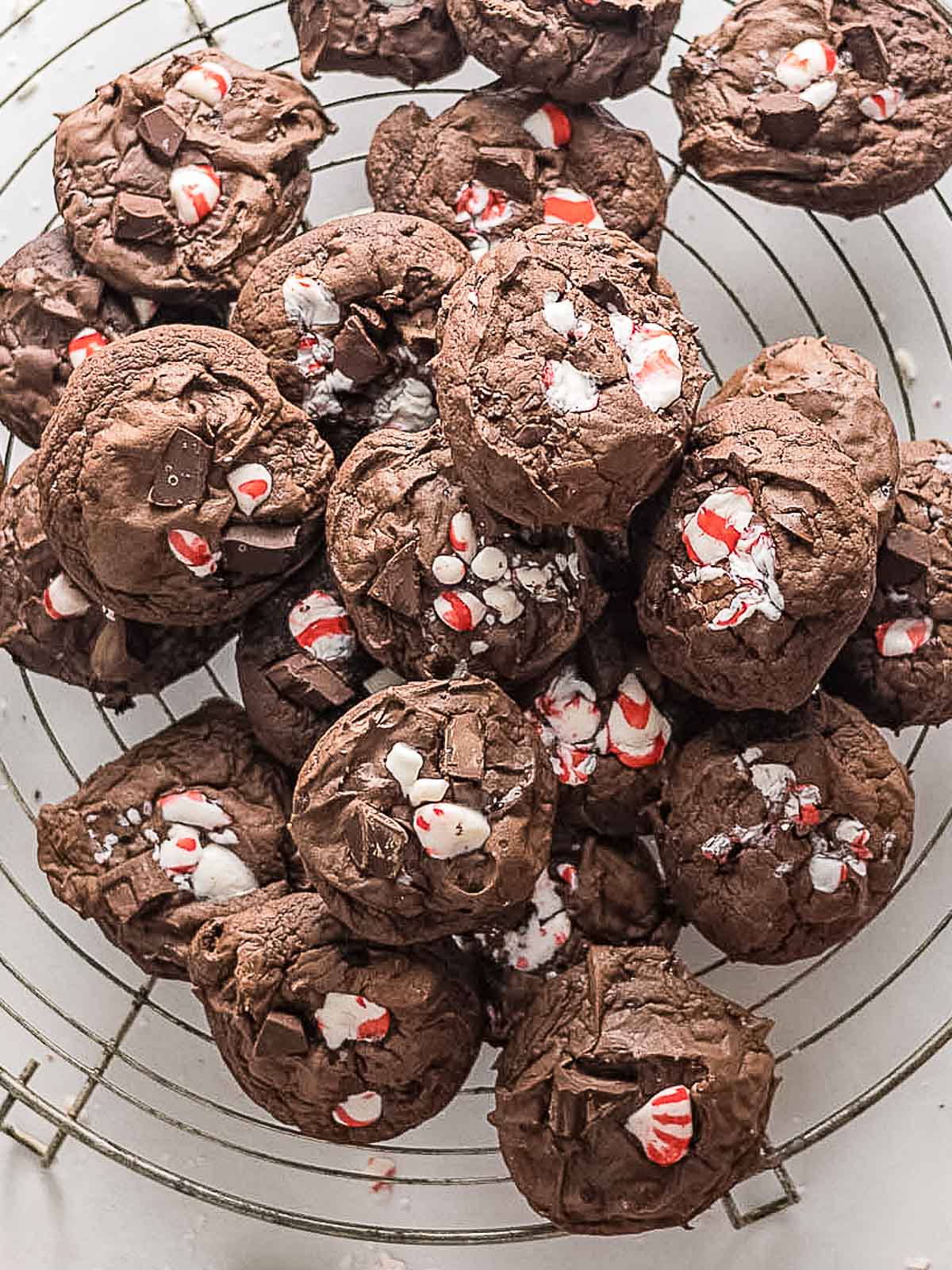 A pile of chocolate cookies with crushed peppermint candy pieces on top, arranged on a round cooling rack.