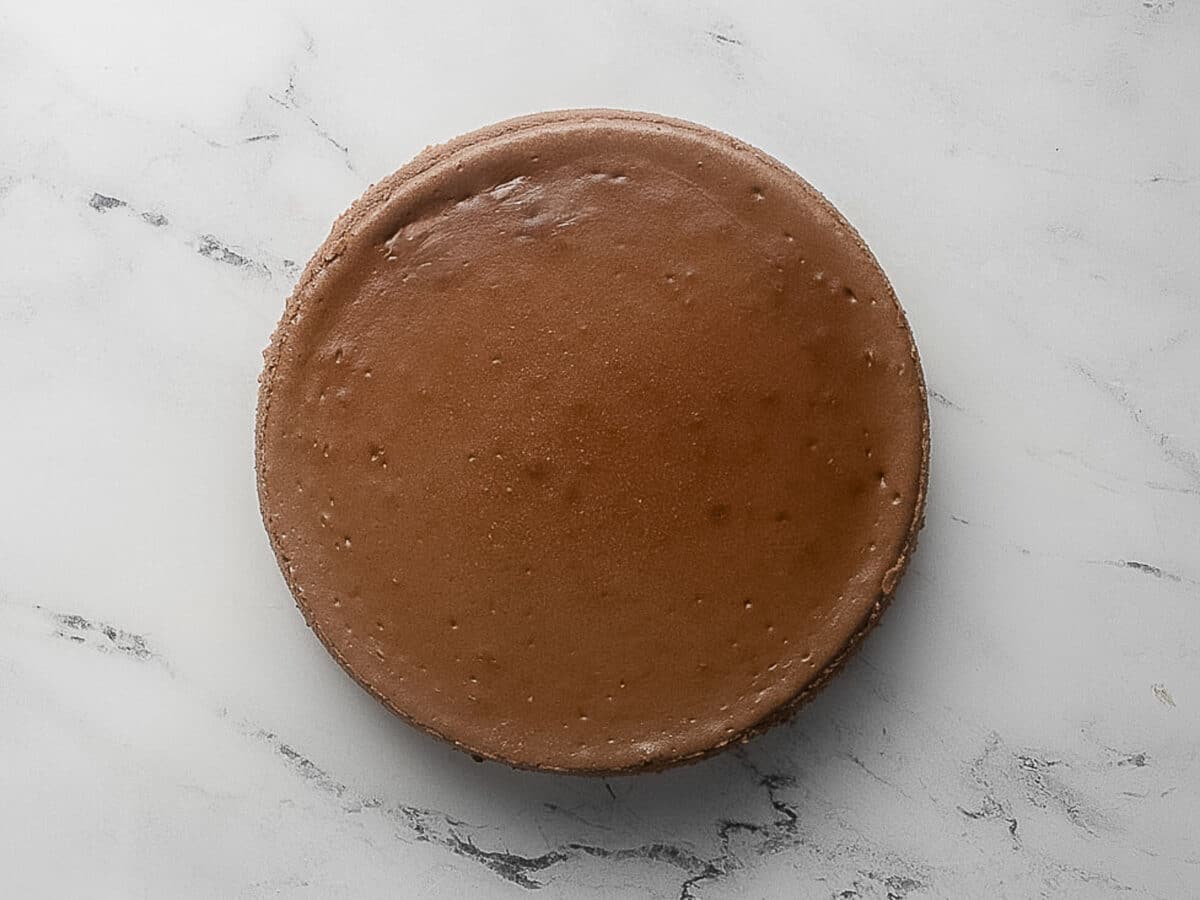 A whole, plain chocolate cheesecake on a white marble surface, photographed from above.
