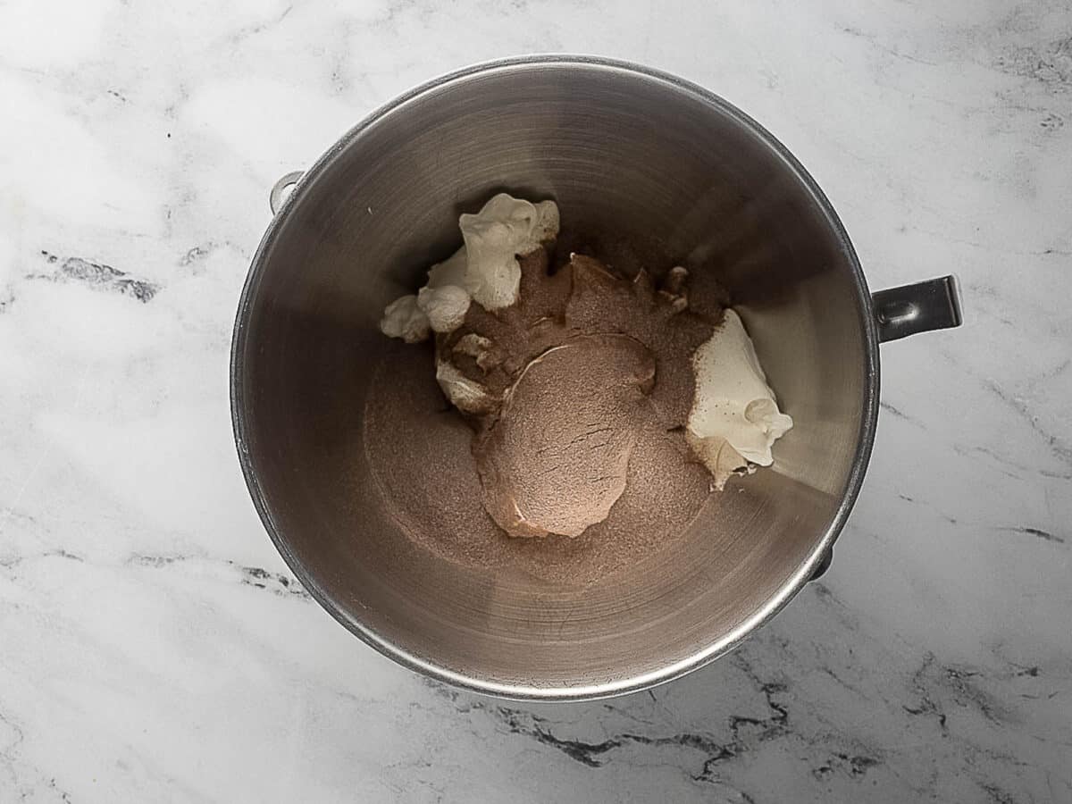 A mixing bowl containing brown sugar and softened butter on a marble countertop.