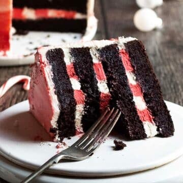 A slice of layered chocolate cake with white and red filling sits on a white plate with a fork.