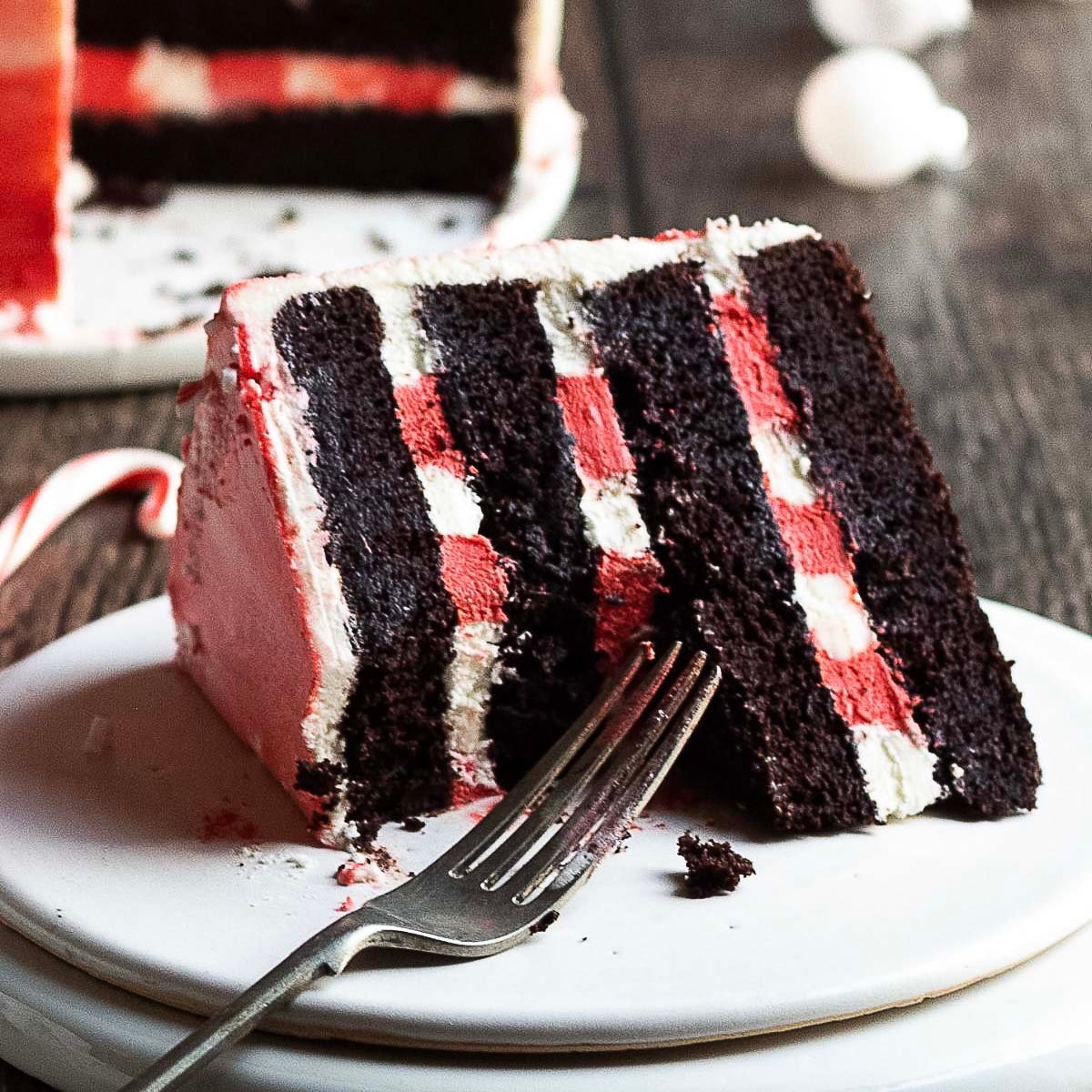 A slice of layered chocolate cake with white and red filling sits on a white plate with a fork.