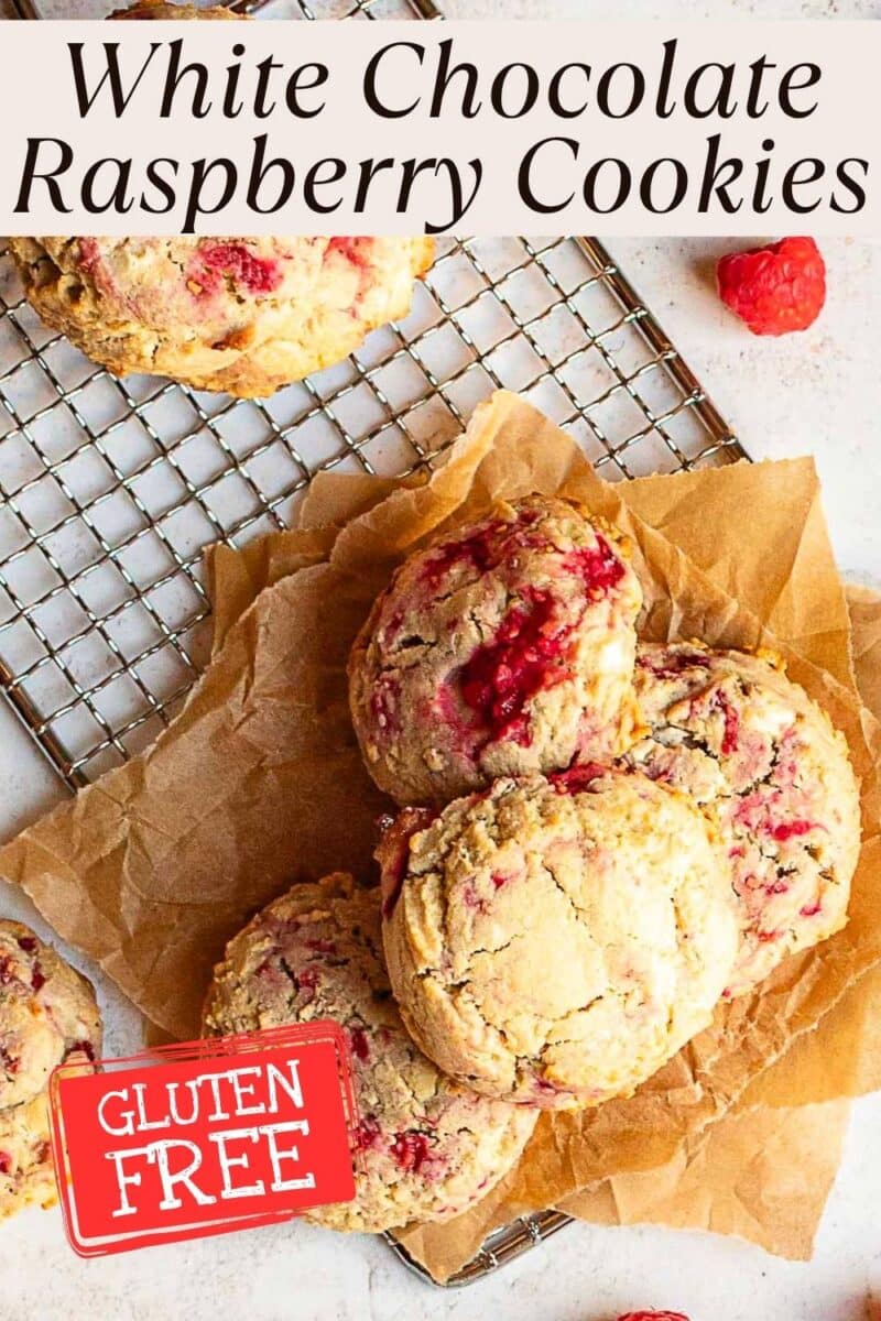 A batch of gluten free raspberry cookies with white chocolate sits on parchment paper and a cooling rack, each labeled as gluten-free.