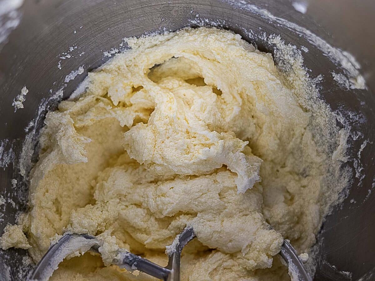 Creamed butter and sugar mixture in a metal mixing bowl with paddle beaters partially visible at the bottom.