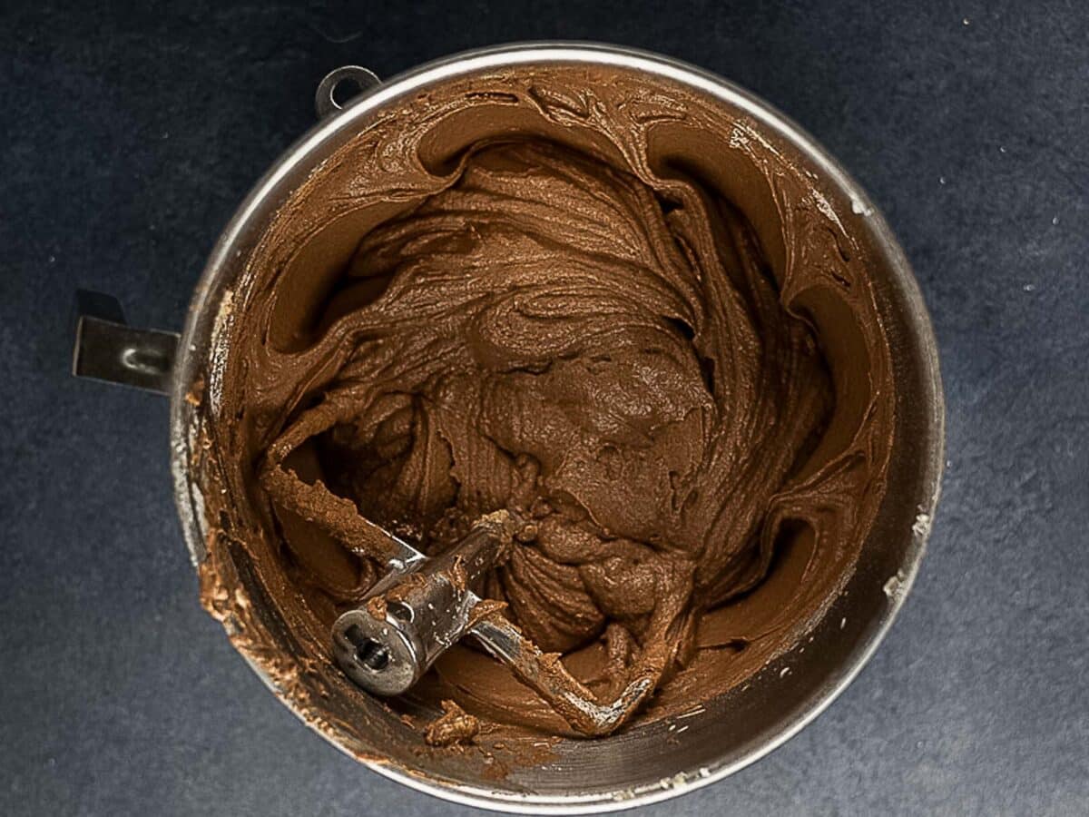 A mixing bowl filled with chocolate cake batter sits on a dark countertop.