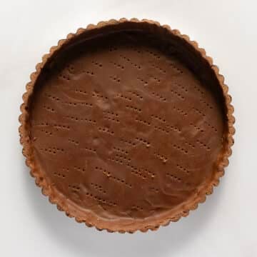 Unbaked chocolate tart crust with fork marks in a fluted tart pan, viewed from above on a white surface.