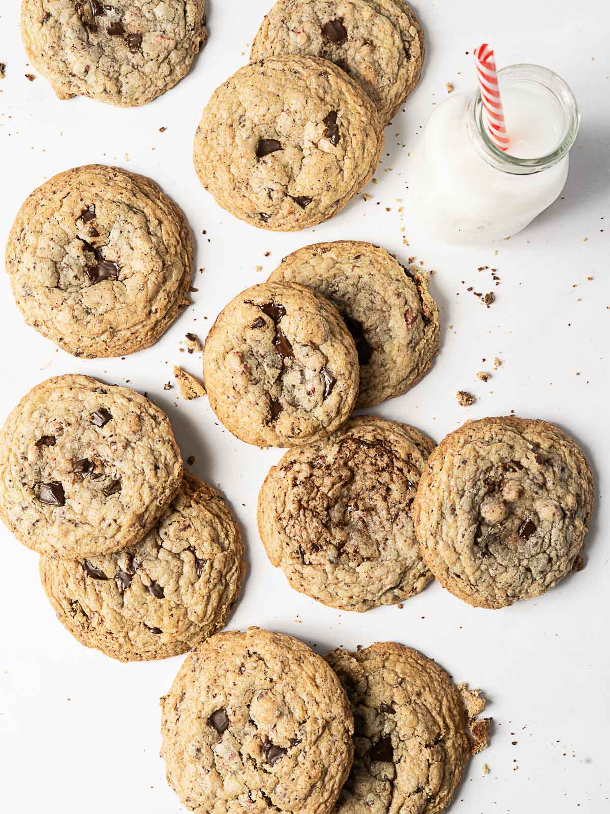 A group of chocolate chip cookies arranged on a white surface next to a bottle of milk with a red and white striped straw.