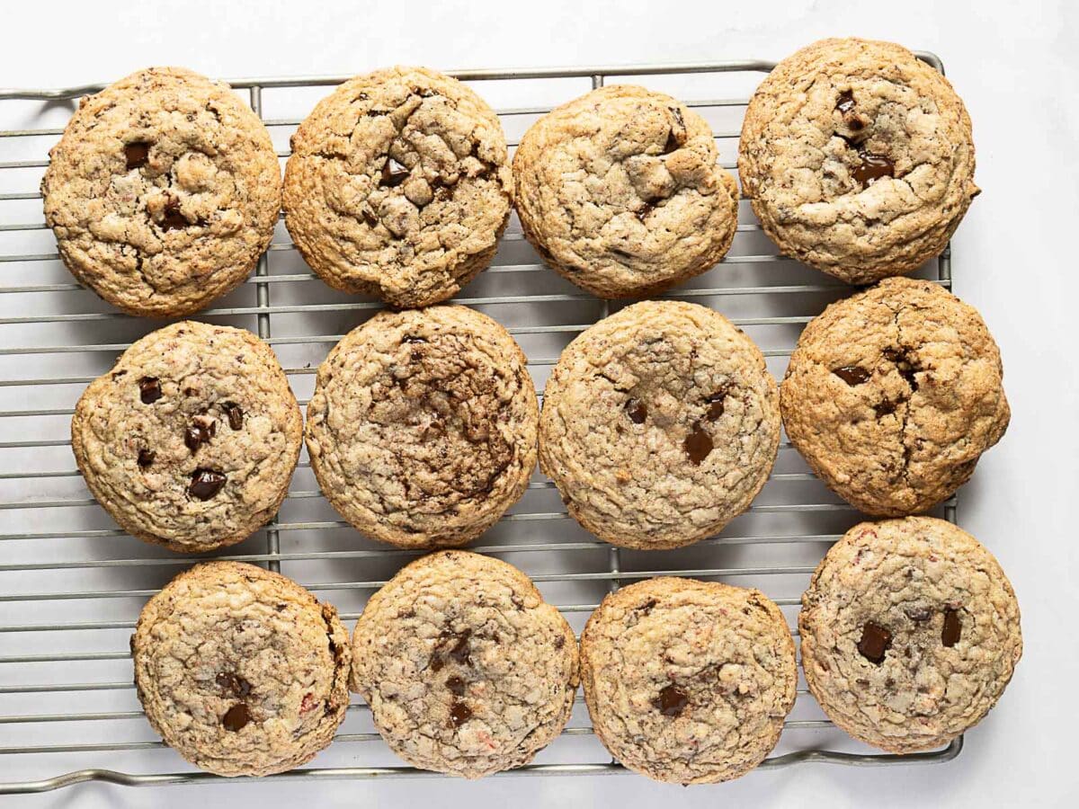 Twelve chocolate chip cookies cooling on a wire rack, arranged in three rows of four, on a white surface.