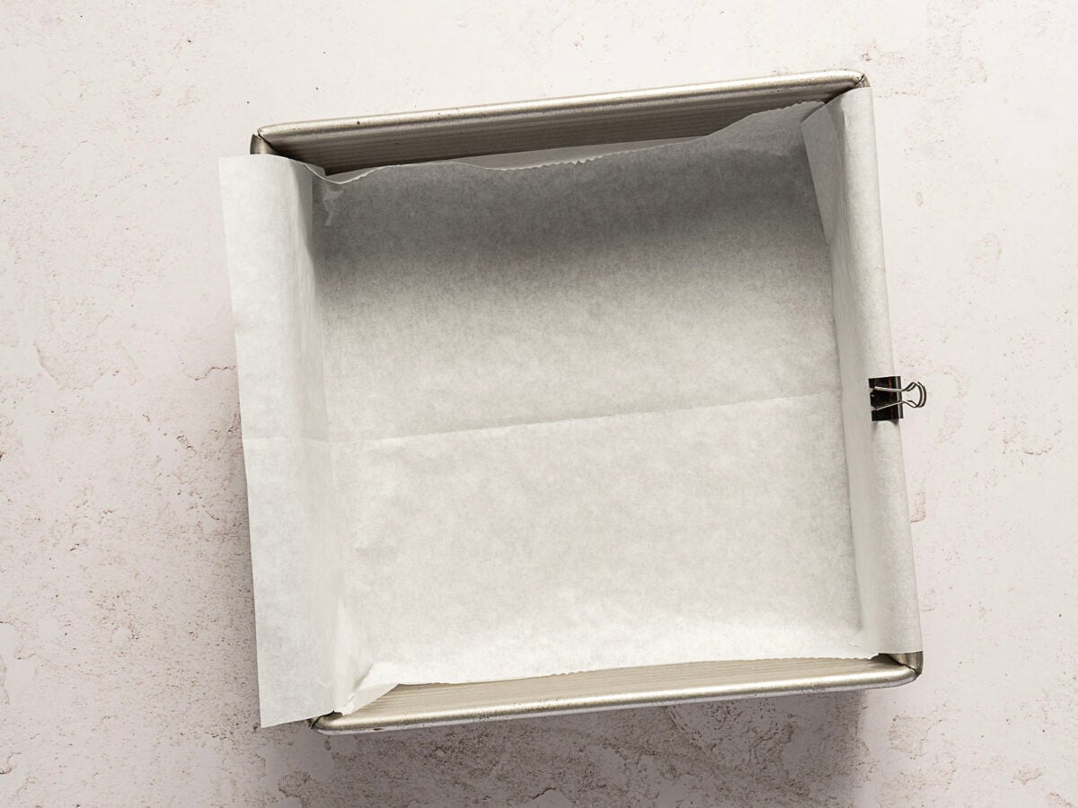 A square baking pan lined with parchment paper, secured by a metal binder clip-perfect for making a no bake chocolate cake or an easy 3 ingredient chocolate cake.
