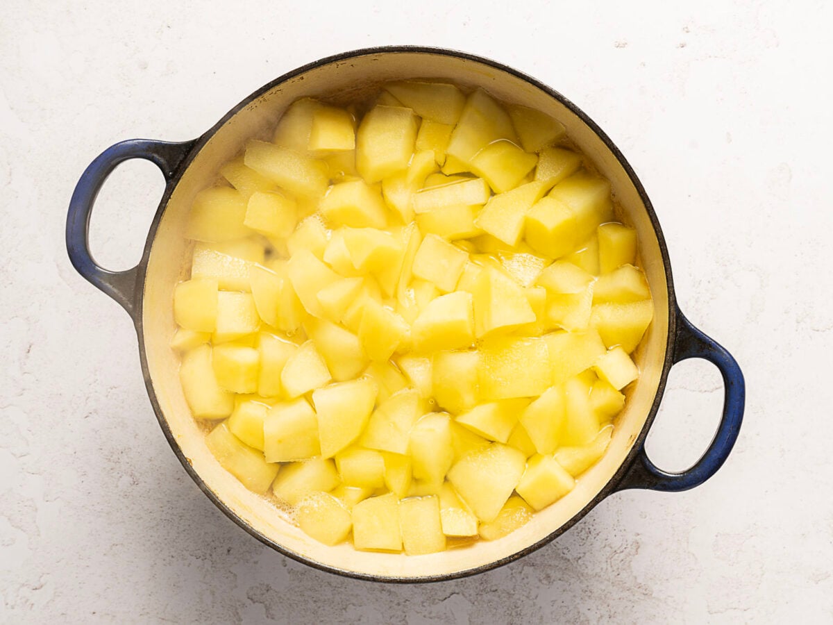 A pot filled with peeled and chopped yellow potatoes cooking in water sits on a light-colored surface-nothing like a no bake 3 ingredient chocolate cake, but just as comforting.