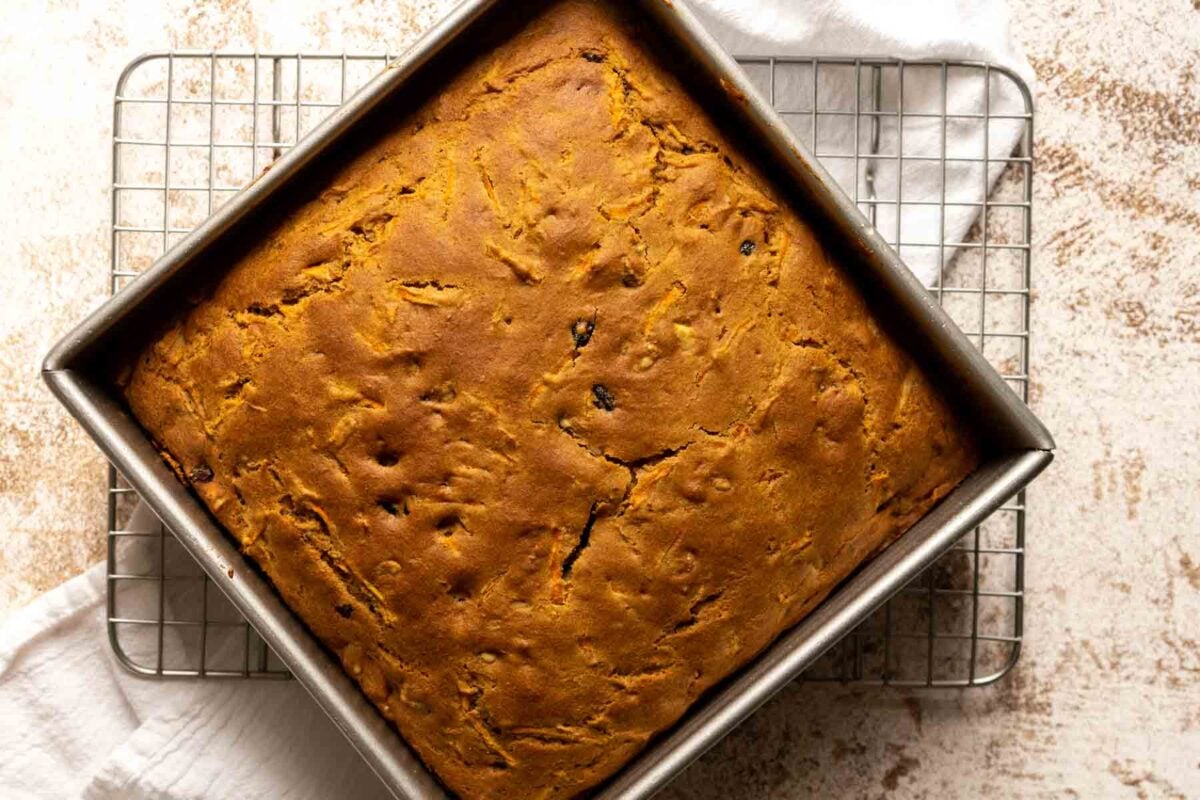 A square pan of gluten free, dairy free carrot cake cools on a wire rack over a white cloth.