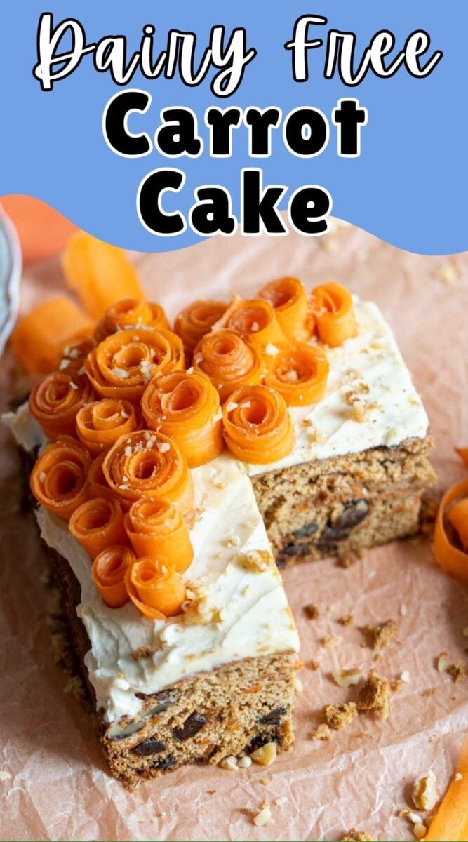 A slice of dairy-free carrot cake topped with cream and decorative carrot ribbons, placed on parchment paper.
