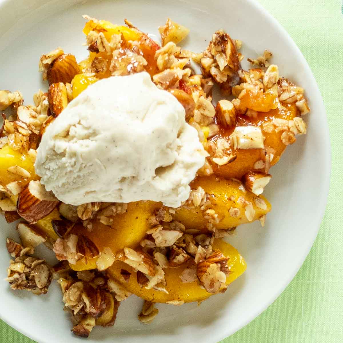 A plate of peach crisp topped with vanilla ice cream, featuring baked peaches, oats, and chopped nuts on a white dish.