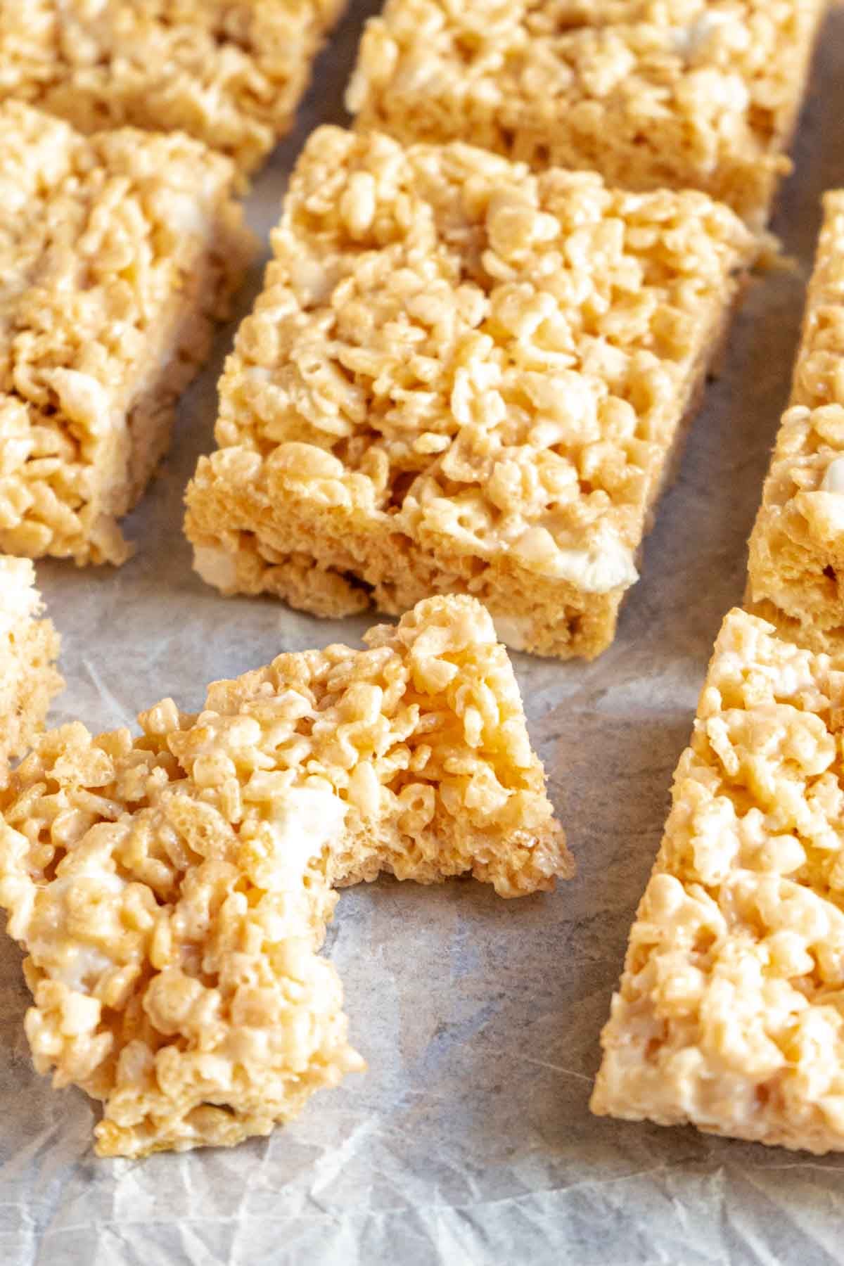 Rectangular gluten free rice krispy treats arranged on parchment paper, with one treat in the foreground showing a bite taken out of it.