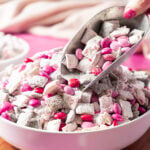 A bowl of powdered sugar-coated snack mix with pink, red, and purple candy-coated chocolates.