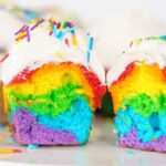 A sliced Rainbow Cupcake with vibrant layers, topped with white frosting and colorful sprinkles—a delightful treat made easy with your favorite cake mix.
