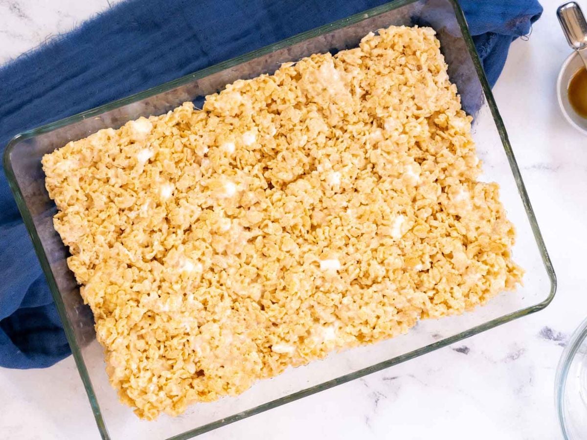 A glass baking dish filled with gluten free rice krispy treats, placed on a blue cloth on a white surface.