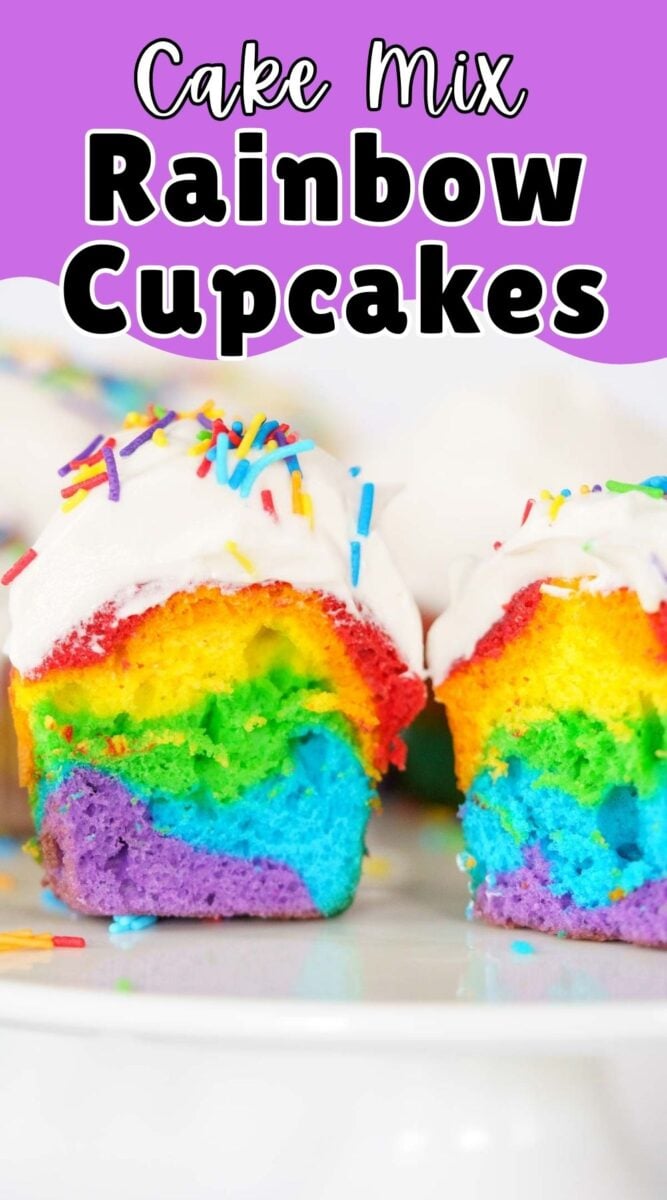 A sliced rainbow cupcake with colorful layers and white frosting topped with rainbow sprinkles sits on a white surface.