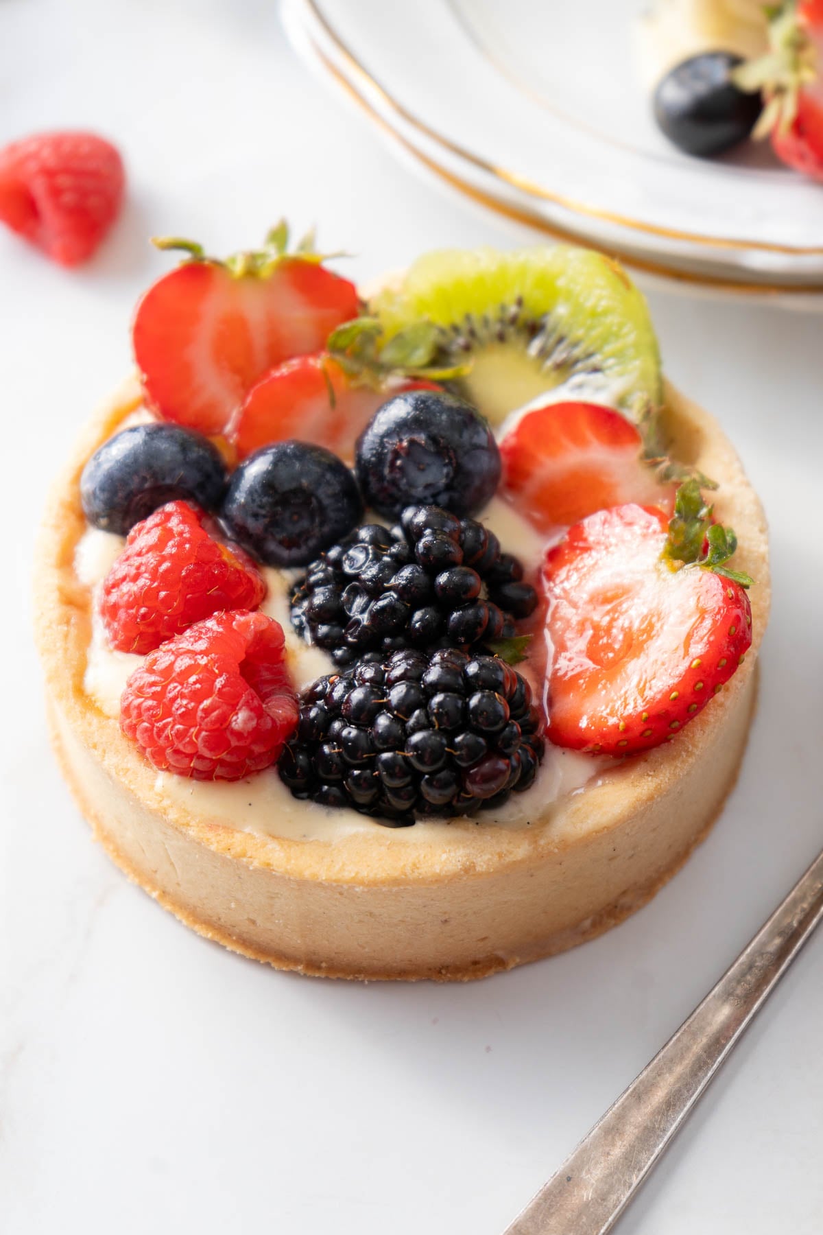 A small cheesecake topped with fresh strawberries, raspberries, blueberries, blackberries, and kiwi slices on a white surface.