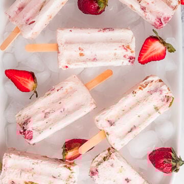 Rectangular strawberry popsicles with wooden sticks are arranged on a bed of ice, surrounded by fresh strawberries and strawberry halves.