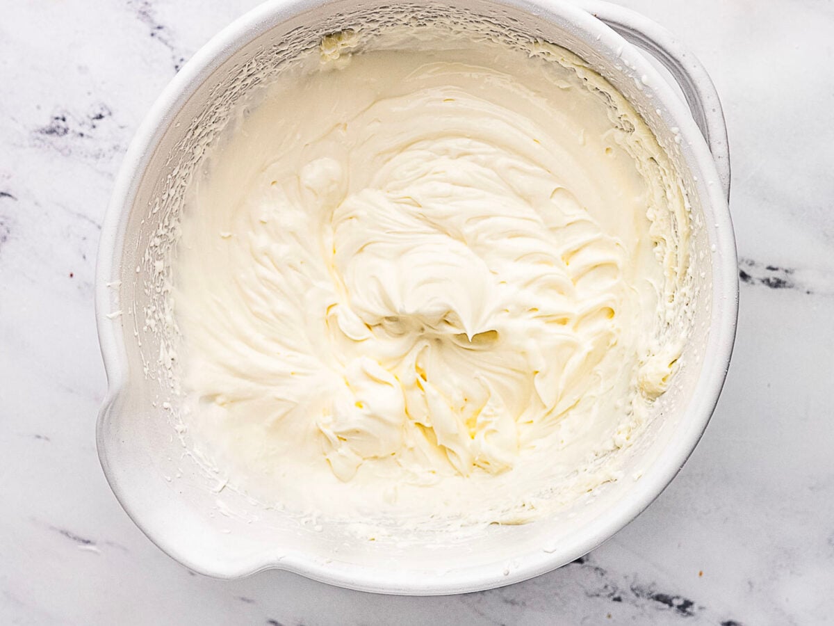 A white mixing bowl filled with thick, creamy whipped mixture sits on a marble countertop.