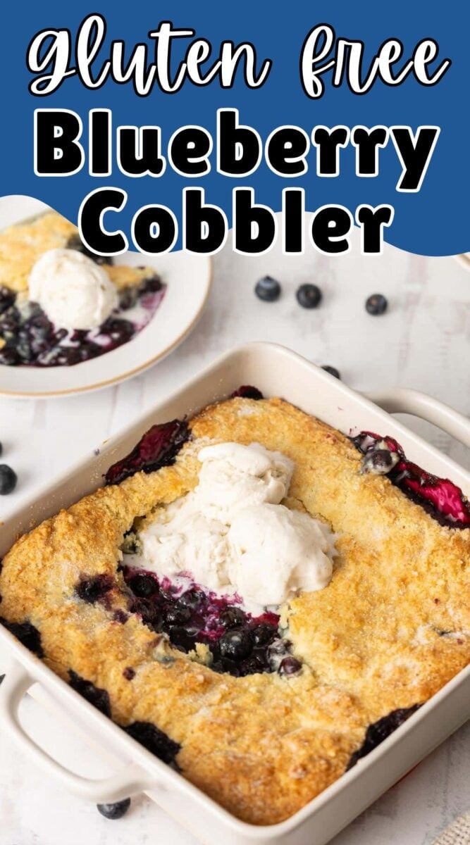 A square baking dish of gluten free blueberry cobbler topped with vanilla ice cream sits on a table, with a serving on a plate in the background.