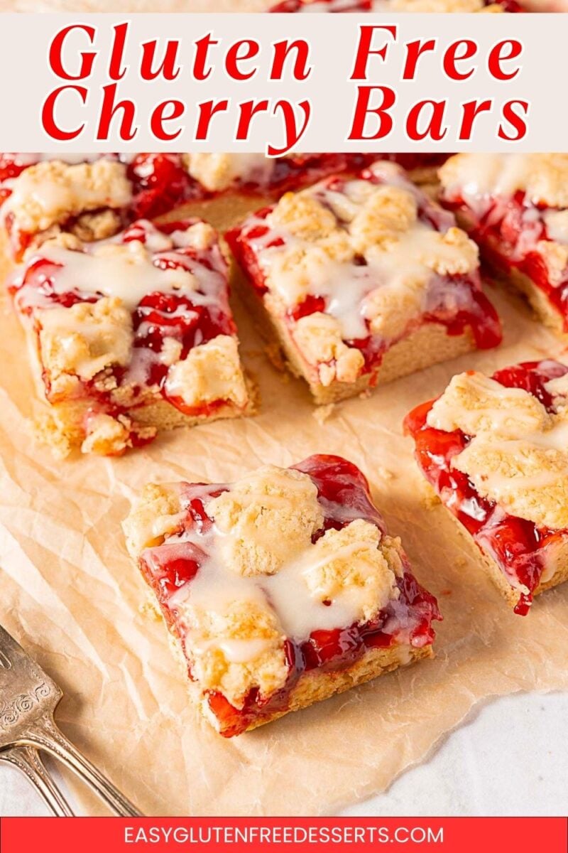 Six gluten free cherry pie bars topped with icing are arranged on parchment paper. The bars display a crumbly texture with visible cherry filling.