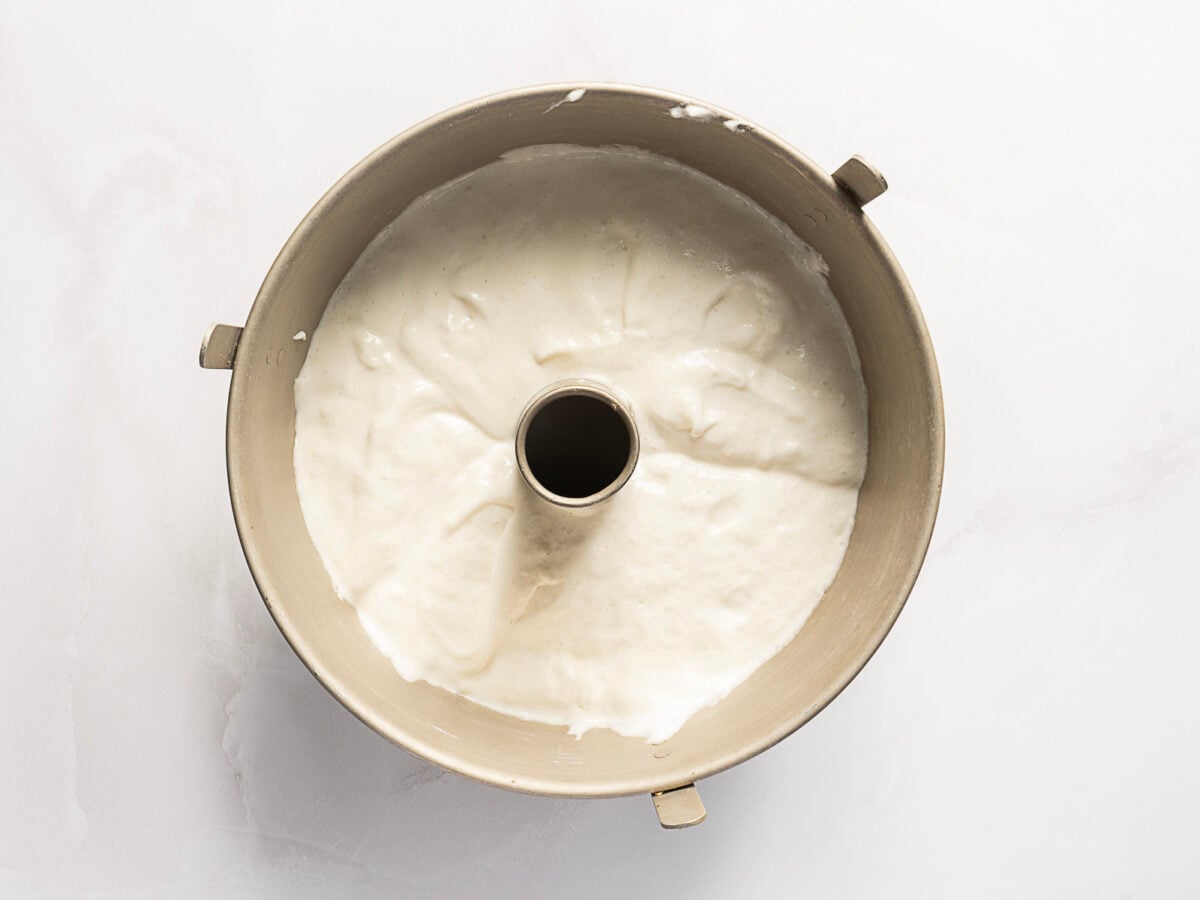 A metal tube pan filled with raw cake batter, photographed from above on a light surface.
