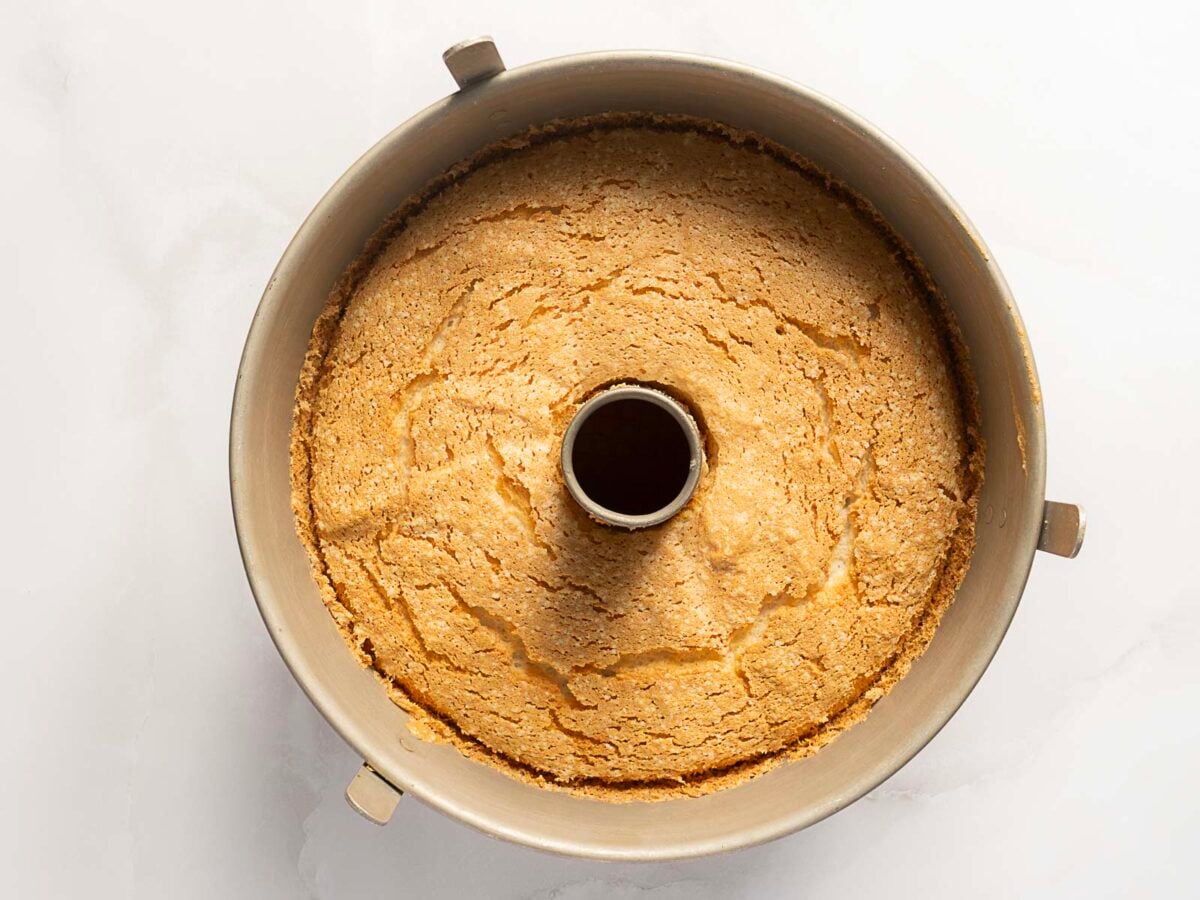 A plain, golden-brown cake baked in a metal tube pan, shown from above on a white surface.