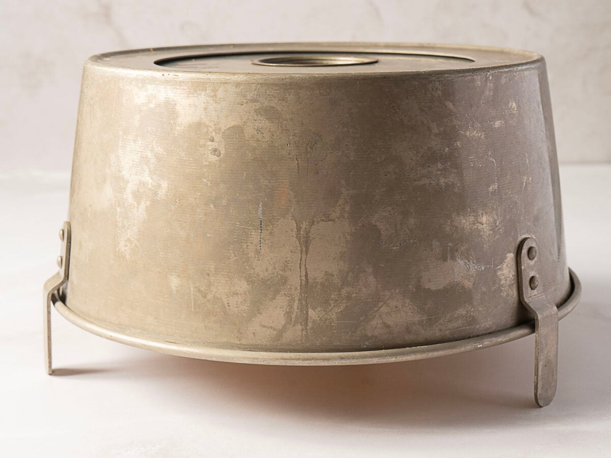 A metal angel food cake pan turned upside down, showing its three metal legs and central tube against a neutral background.