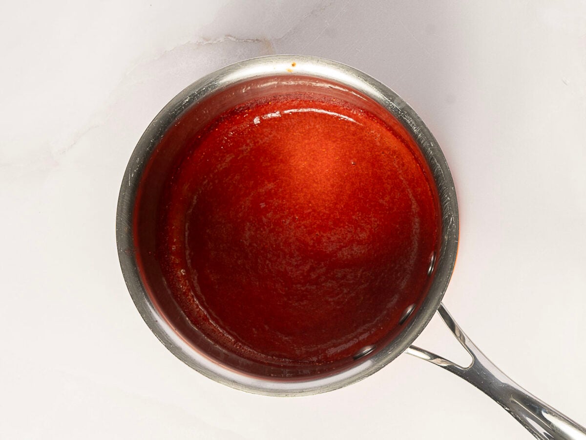 A metal saucepan filled with smooth, red sauce sits on a white surface.