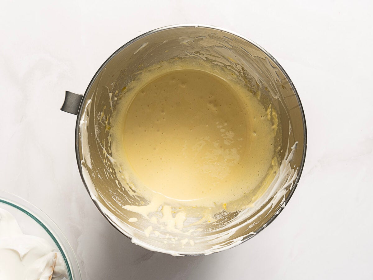A metal mixing bowl containing a smooth, pale yellow batter mixture, with some batter splattered on the sides of the bowl.