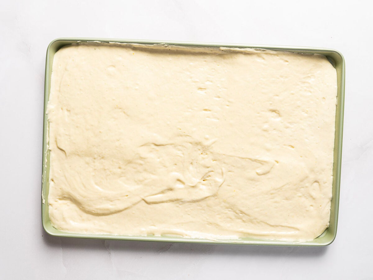 A rectangular baking pan filled with an even layer of unbaked cake batter, shown from above on a white surface.