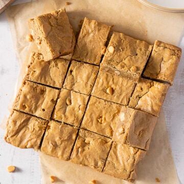 A batch of blondies cut into 16 square pieces, some pieces slightly separated, with visible butterscotch chips on top and parchment paper underneath.