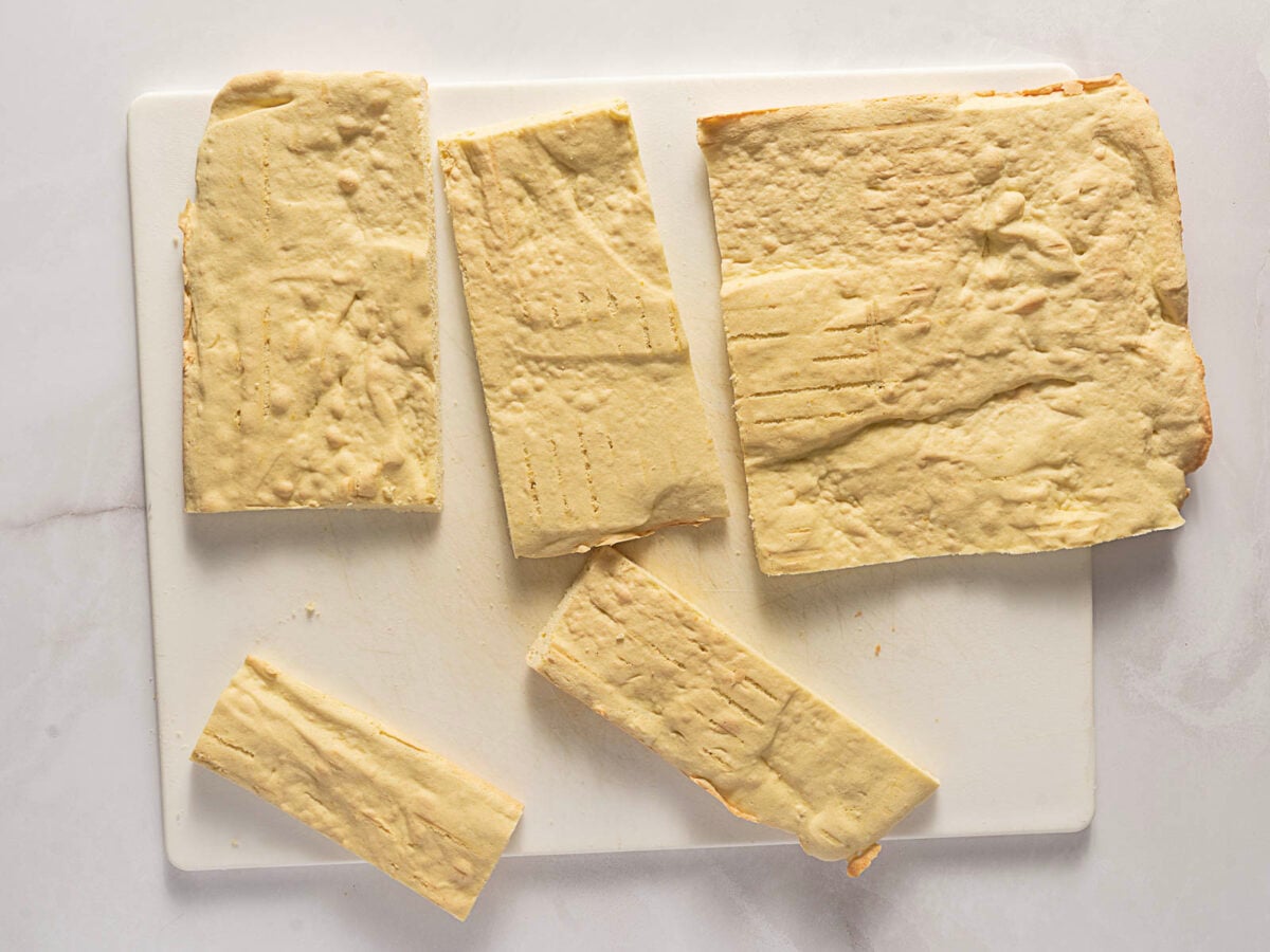Several rectangular pieces of plain baked cake are arranged on a white cutting board atop a light-colored surface.