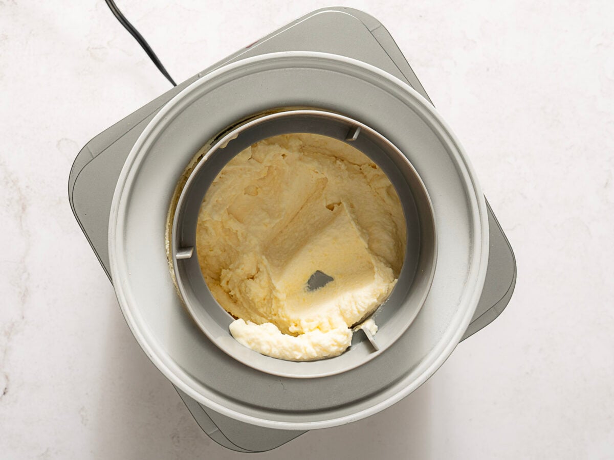 Overhead view of an ice cream maker with partially churned vanilla ice cream inside.
