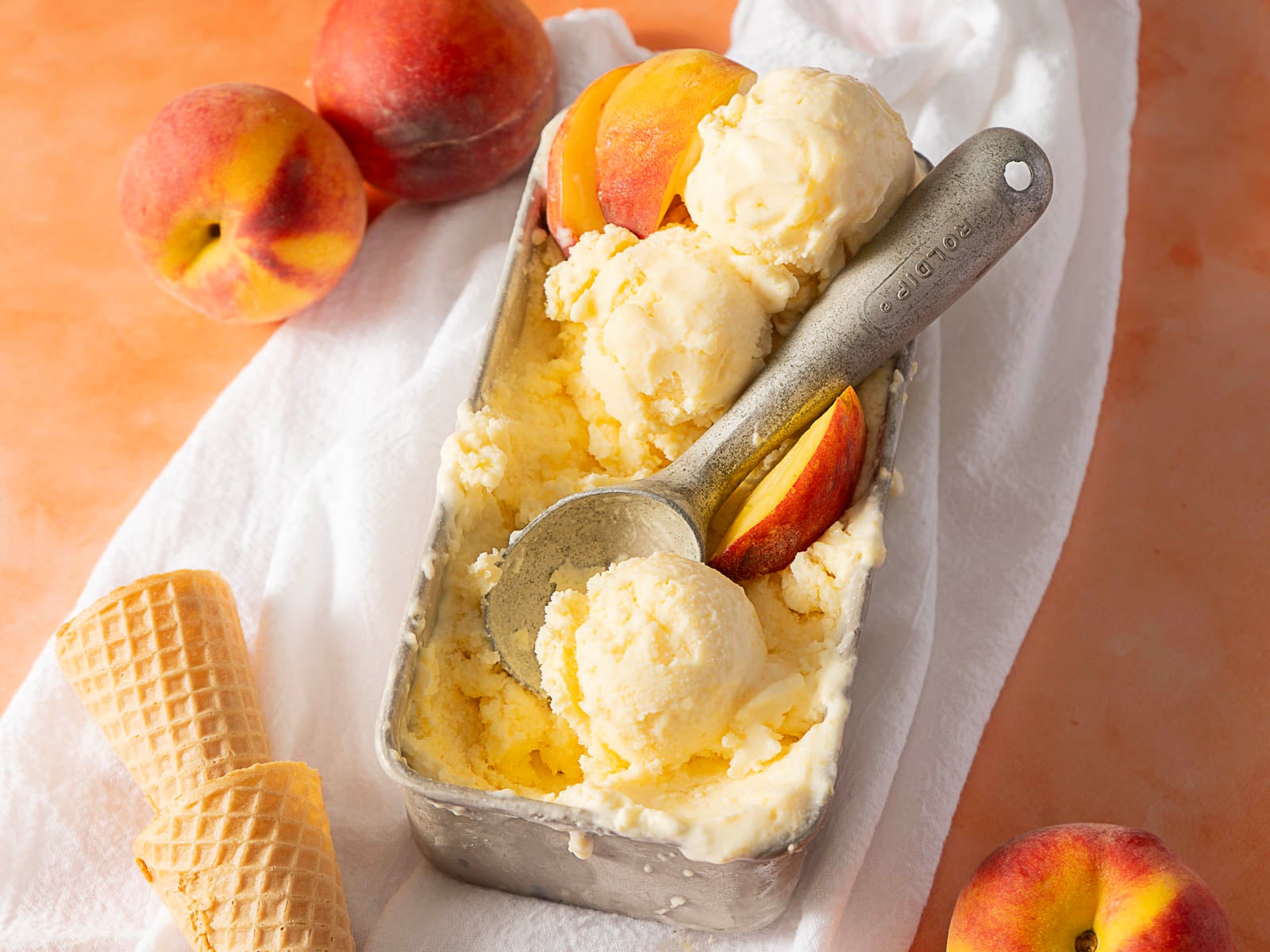 A pan of peach ice cream with a scoop and fresh peaches.