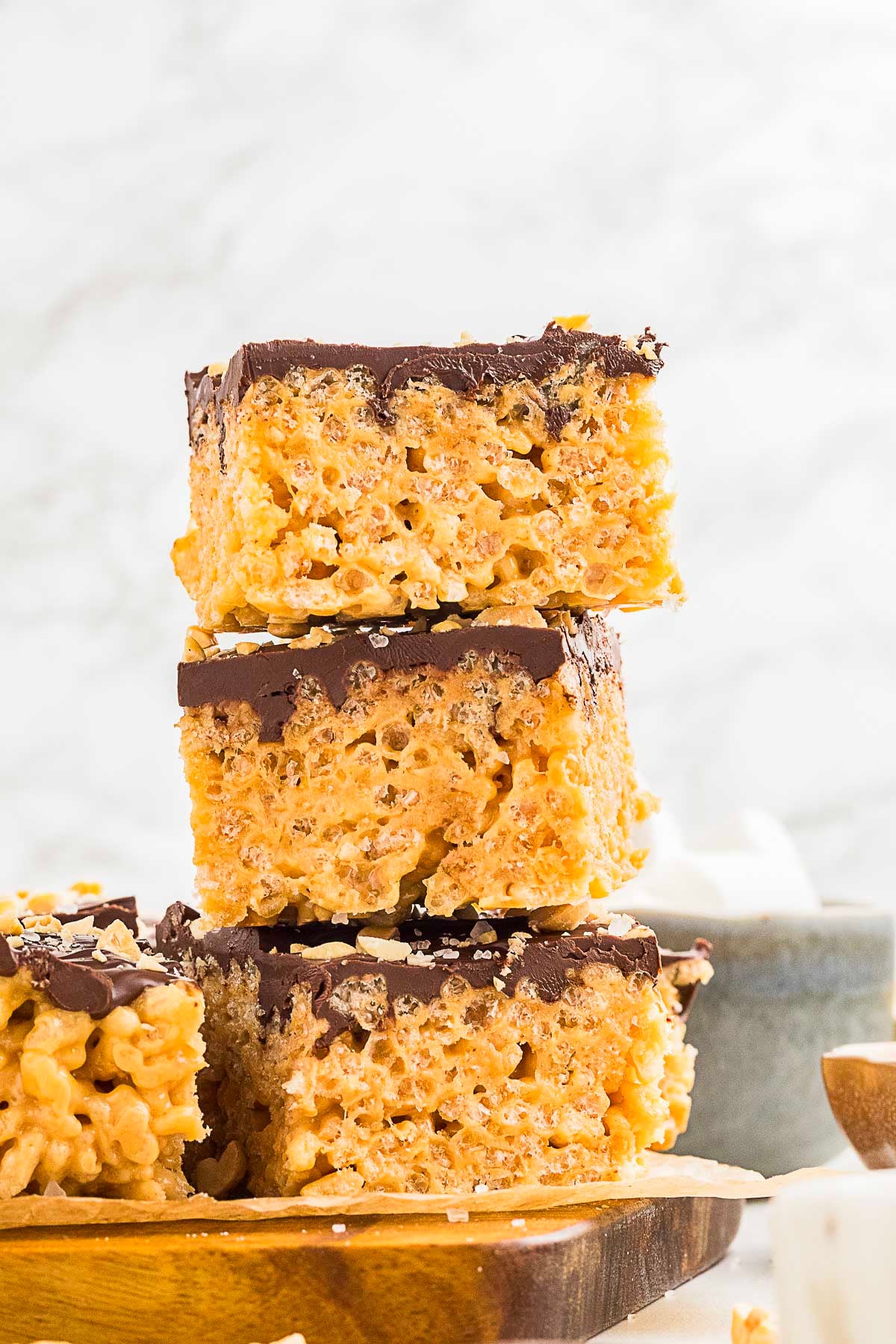 Three stacked rice crispy treats topped with a layer of chocolate, displayed on a wooden board with a blurred background.
