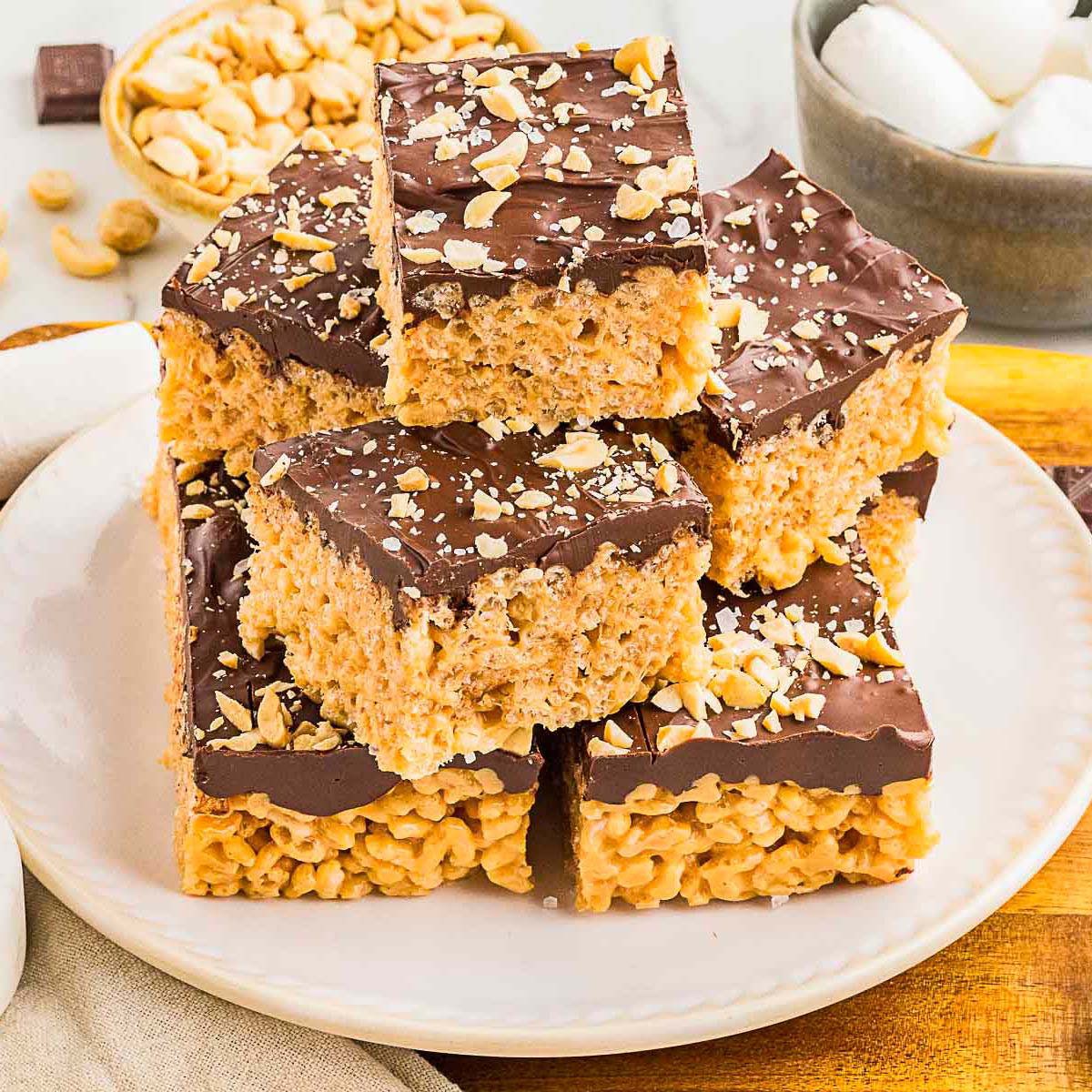 A plate of rice crispy treats topped with a layer of chocolate and chopped peanuts, stacked on top of each other.