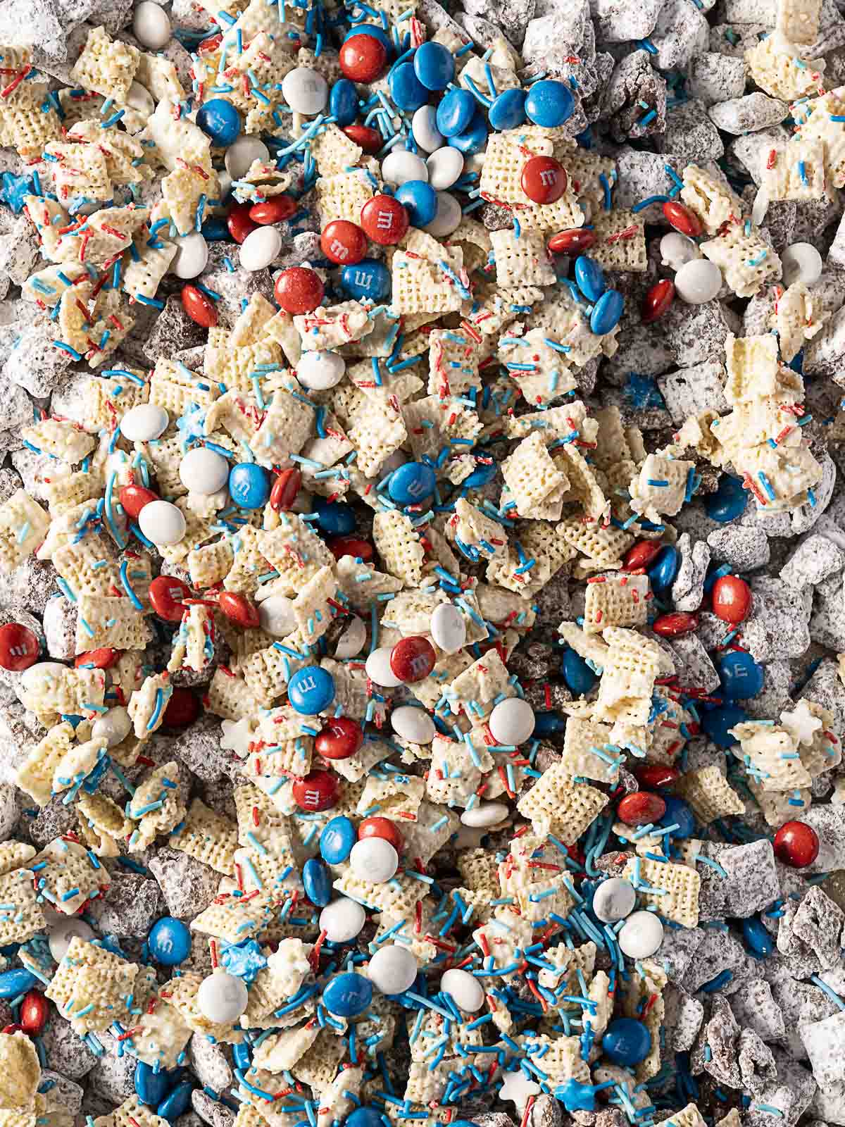 Close-up of a snack mix with Chex cereal, powdered sugar, red, white, and blue M&Ms, and red and blue sprinkles.