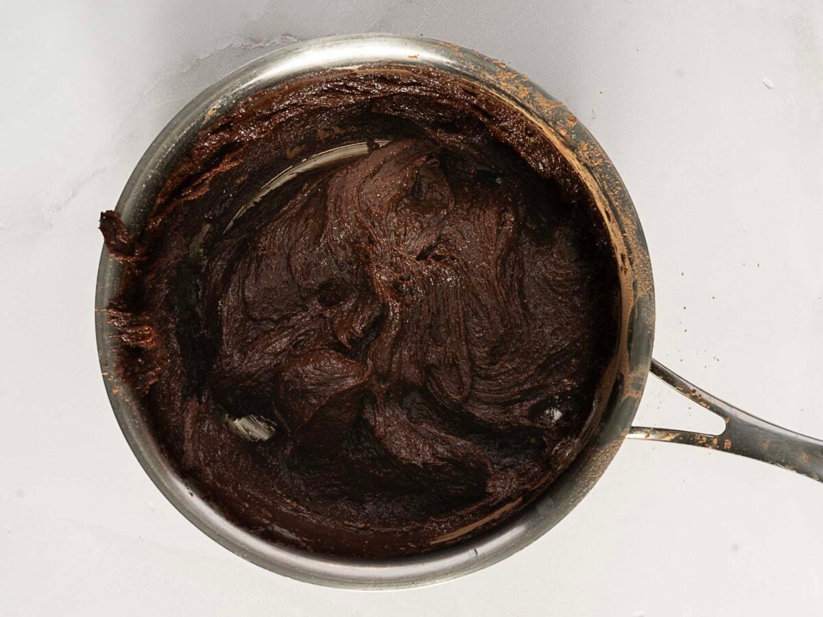 A saucepan containing thick, dark chocolate batter is shown from above on a light surface.
