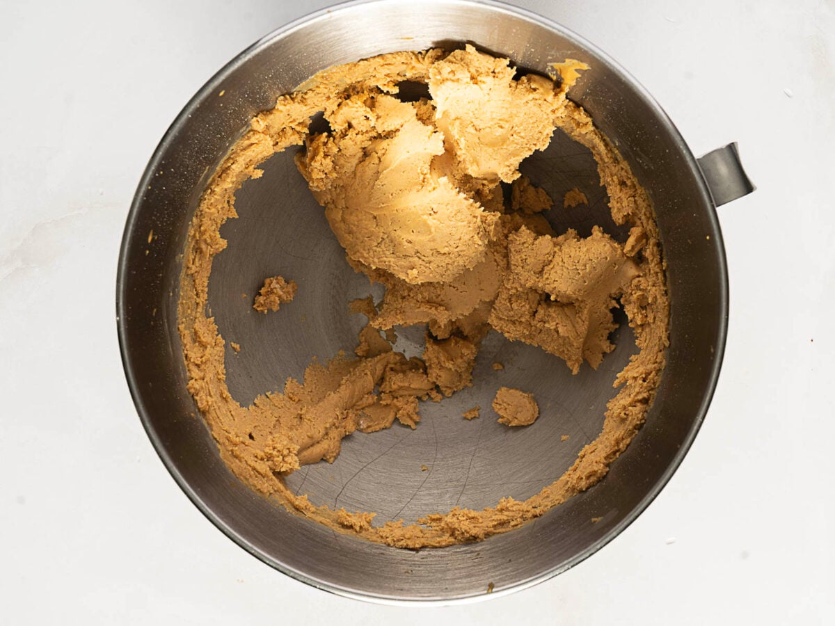 A metal mixing bowl containing partially mixed cookie dough sits on a light countertop.